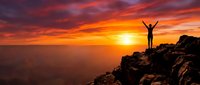 Silhouette of person with raised arms celebrating success on mountain peak at dramatic sunset with vibrant orange and red sky over vast landscape horizon.