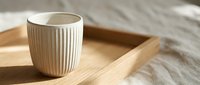 Ceramic cup with vertical ribbed texture on wooden tray, minimalist tableware styling for home decor and lifestyle content.