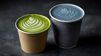 Green matcha latte with leaf art pattern in kraft cup and blue spirulina latte in black cup on dark background, trendy specialty coffee alternatives.
