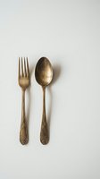 Vintage brass fork and spoon with ornate handles on neutral background for kitchen decor and dining concepts.