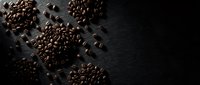 Roasted coffee beans scattered on dark wooden surface creating aromatic cafe atmosphere for beverage and culinary design projects.