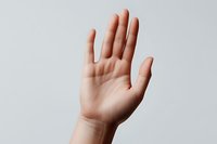 Raised open palm of a young Caucasian person showing stop gesture against light gray background, minimalist composition for conceptual design and communication.