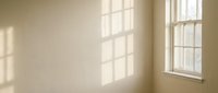 Empty room interior with natural sunlight streaming through large windows creating geometric shadow patterns on beige walls for home design projects.