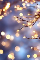 Glowing fairy lights on branches against soft blue background with magical bokeh effect, creating dreamy holiday atmosphere for festive designs.