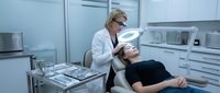 Female dentist examining male patient in modern dental office with professional equipment and clean white interior design for healthcare marketing.