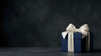 Dark blue gift box with cream ribbon bow on dark textured background, suitable for holiday, celebration, and luxury product marketing designs.