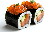 Fresh salmon and cucumber sushi rolls topped with bright orange caviar, garnished with green leaves on white background, close-up view of Japanese cuisine.