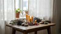 Peaceful spa wellness setup with burning candles, lavender, smooth stones and natural elements on wooden table by window for relaxation and meditation.