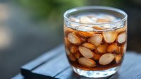 Refreshing cola drink with ice cubes in glass on dark wooden table against blurred background. Close up view of carbonated beverage with bubbles.