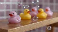 Pink and yellow rubber ducks lined up on wooden surface with floating soap bubbles creating playful bathroom decoration composition for children's bath time fun.