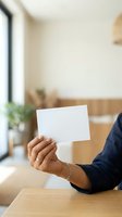Person with medium skin tone holding blank white card at wooden desk in modern office with natural light, suitable for business, marketing, and corporate messaging concepts.