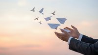 Businessman hands releasing paper airplanes transforming into flying birds at sunset symbolizing freedom, success, and business growth concepts.