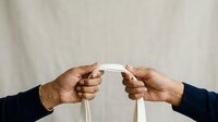 Two people exchanging a white business card against neutral background. Suitable for corporate communication, networking, professional meetings, and business transaction concepts.