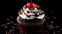 Chocolate cupcake topped with swirled vanilla frosting, chocolate drizzle, sprinkled chocolate chips and bright red maraschino cherry on dark background.