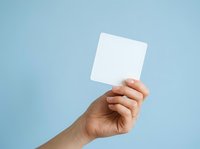 Hand holding blank white card against light blue background, suitable for mockups, advertising, and promotional designs.