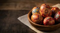 Traditional painted Easter eggs with intricate folk patterns in wooden bowl on rustic table for spring holiday celebration and cultural decoration.