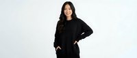 Young Asian woman in casual black sweatshirt and pants standing confidently with hands on hips, smiling at camera on white background for lifestyle content.