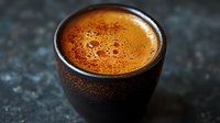 Fresh espresso with golden crema in dark ceramic cup on textured black surface, close up view with selective focus and moody lighting.