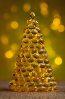 Golden capsules stacked in Christmas tree shape against warm bokeh background, creating festive holiday concept for health and wellness marketing.