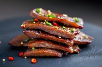 Glazed pork ribs with herbs and spices on dark slate surface. Barbecue meat with caramelized coating garnished with fresh green herbs and peppercorns.