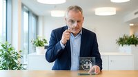 Mature Caucasian businessman in navy suit examining water with magnifying glass in modern office environment for quality control analysis.