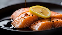 Fresh raw salmon fillets with lemon slice and olive oil drizzle on black plate, garnished with black pepper, close up view of gourmet seafood preparation.