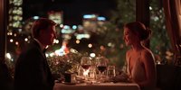 Elegant couple enjoying romantic dinner date at upscale restaurant with city lights bokeh background creating intimate atmosphere for anniversary celebration.