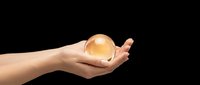 Female hands holding glowing golden orb sphere on black background for mystical energy healing meditation spiritual wellness concepts.