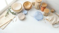 Flat lay arrangement of eco-friendly storage containers, glass jars, wooden spoons, and reusable fabric bags on white background for sustainable living and zero waste lifestyle concepts.