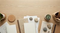 Minimalist workspace flat lay on wooden desk with notebooks, pebbles, succulents, and cork coasters, top view with copy space.