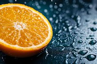 Fresh juicy orange half with water drops and splashes on dark background, dramatic lighting creates appetizing citrus fruit composition for food design.
