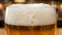 Frothy beer with thick foam head in glass, golden amber liquid with condensation droplets, bar setting background, beverage and refreshment concept.