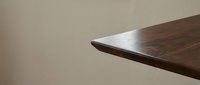 Modern walnut wood table corner with smooth grain pattern against neutral wall background for interior design projects.
