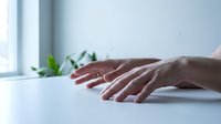 Professional hands typing on white keyboard in modern office workspace with natural lighting and green plant background for business productivity.