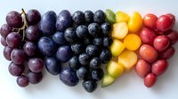 Fresh colorful fruits arranged in rainbow pattern with red grapes, blueberries, yellow mango chunks and red radishes on white background, healthy eating concept.