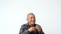 Middle-aged man with gray hair and facial hair, appearing to be of Latin American descent, wearing a blue plaid shirt, speaking or presenting with microphone against white background.