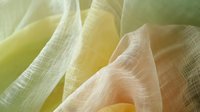 Delicate folds of translucent fabric in soft yellow and cream tones create an ethereal abstract composition with gentle curves and flowing lines, suitable for luxury fashion backgrounds.
