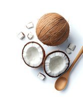 Fresh coconut halves and whole nut with white flesh pieces scattered on white background, wooden spoon for tropical food styling and recipe photography.