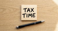 Tax time reminder note with pen on wooden desk for accounting and financial planning preparation during filing season.