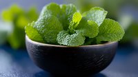 Fresh green mint leaves in black ceramic bowl on dark background, aromatic herbs for cooking, cocktails and tea preparation, macro food photography.