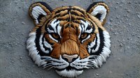 Detailed embroidered tiger head patch with textured fur effect and dimensional design on gray background, featuring orange, white and black thread work.