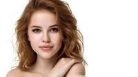 Young woman with natural makeup and wavy brown hair smiling confidently against white background, bare shoulders showing. Professional beauty portrait with soft lighting.