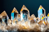 Clear quartz crystal points cluster with natural formations and rainbow light reflections on dark background for healing and meditation practices.