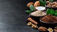 Ground spices and nuts arrangement with cocoa powder, cinnamon sticks, walnuts and fresh mint leaves on dark background with copy space for baking and cooking.