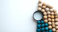 Wooden and turquoise beads arranged in geometric pattern with magnifying glass on white background, minimalist composition for business and analytics concept.