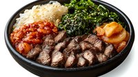 Korean beef bulgogi bowl with marinated sliced meat, steamed rice, seasoned spinach, kimchi and pickled vegetables served in black stone plate for Asian cuisine.