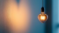 Heart shaped glowing light bulb casting warm illumination against blue wall background, romantic mood lighting creates soft heart shadow pattern.