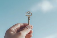 Hand holding vintage golden key against blue sky with soft clouds, symbolizing opportunity, success, and new beginnings.