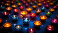 Glowing colorful tea light candles arranged in rows creating atmospheric mood lighting against dark background, flames reflecting on blue surface.