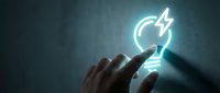 Hand holding glowing neon lightbulb with lightning bolt symbol, representing innovation, creative ideas, energy efficiency and smart solutions for business and technology concepts.